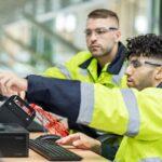 Techniker pruefen Kabelkonfektion und Systemaufbau am Monitor in industrieller Umgebung